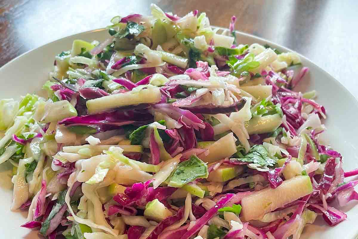 A white bowl filled with apple and cabbage slaw.