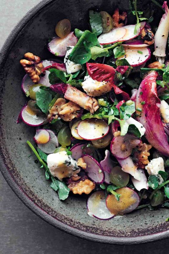 A bowl filled with greens, sliced radish, blue cheese, and toasted nuts.