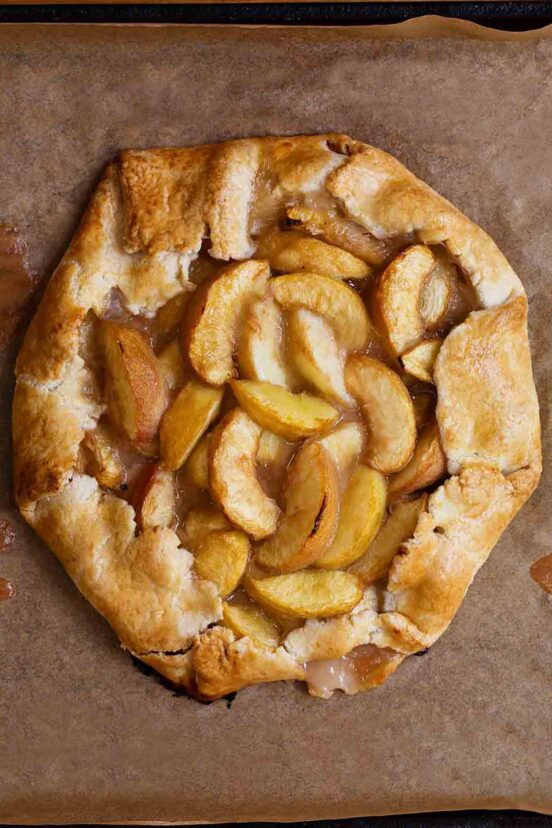 A white peach crostata--slices of white peaches in a circle of dough folded over on the edges sitting a sheet of parchment.