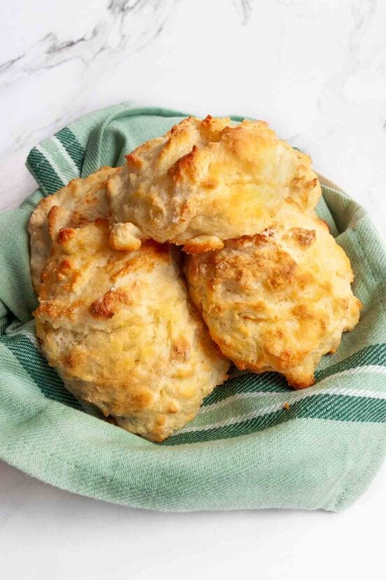 Four buttermilk drop biscuits in a bowl lined with a striped green kitchen towel.