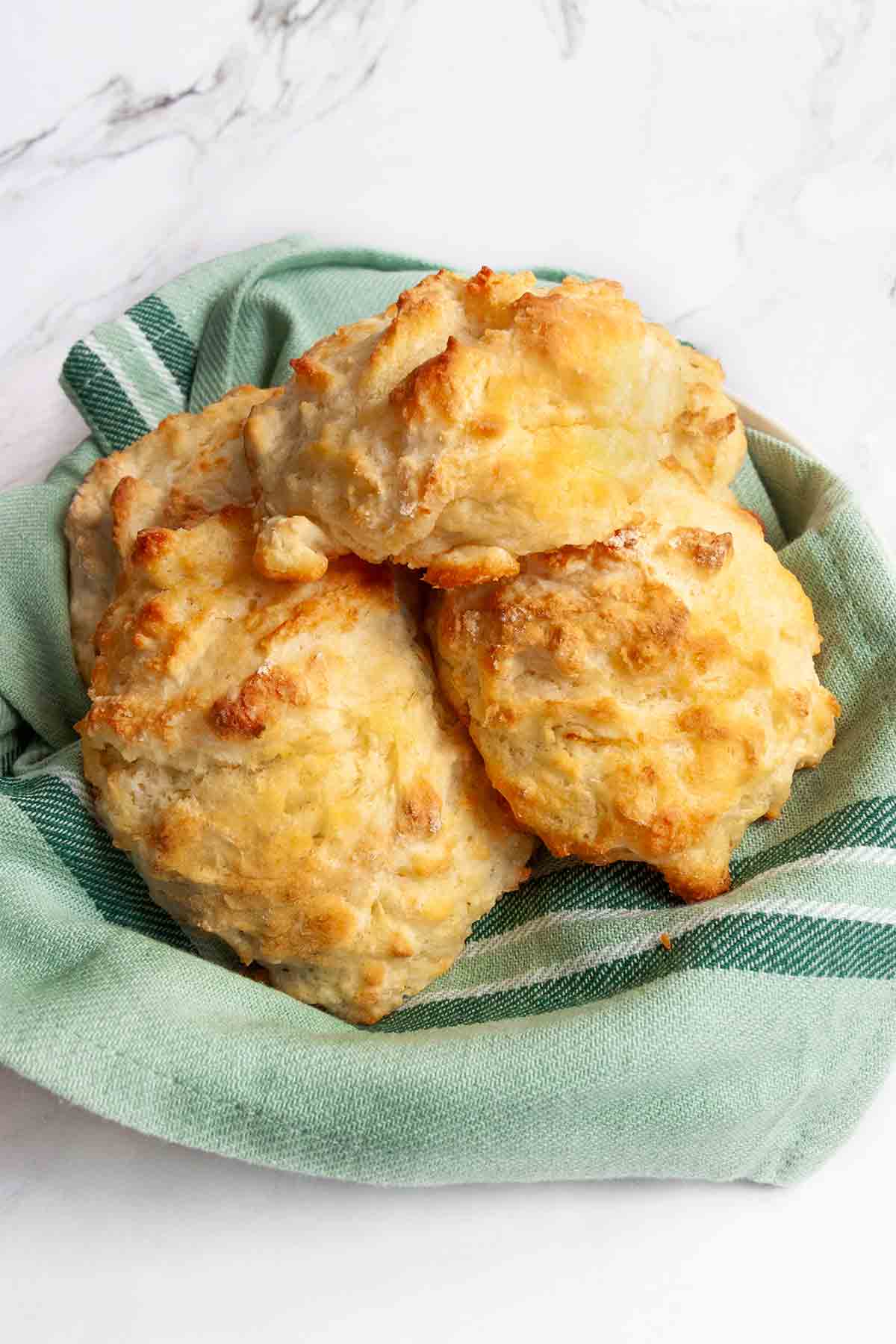 Four buttermilk drop biscuits in a bowl lined with a striped green kitchen towel.
