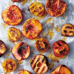 Several halved grilled peaches and plums on a piece of parchment, drizzled with honey and sprinkled with black pepper.