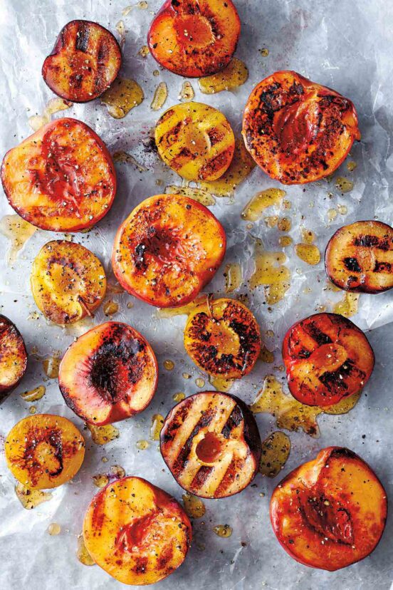 Several halved grilled peaches and plums on a piece of parchment, drizzled with honey and sprinkled with black pepper.