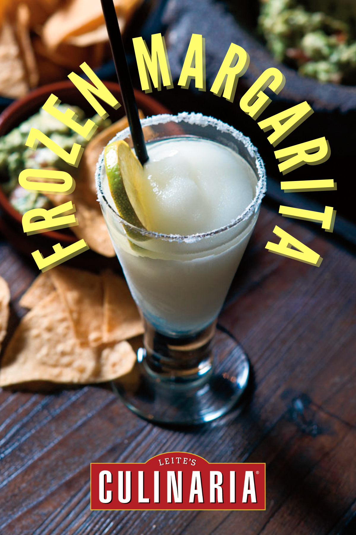 A tall glass of frozen margarita with a salt rim and lime wheel beside a bowl of chips and guacamole.