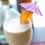 A wine glass filled with frozen Long Island iced tea, garnished with an orange slice on an umbrella.