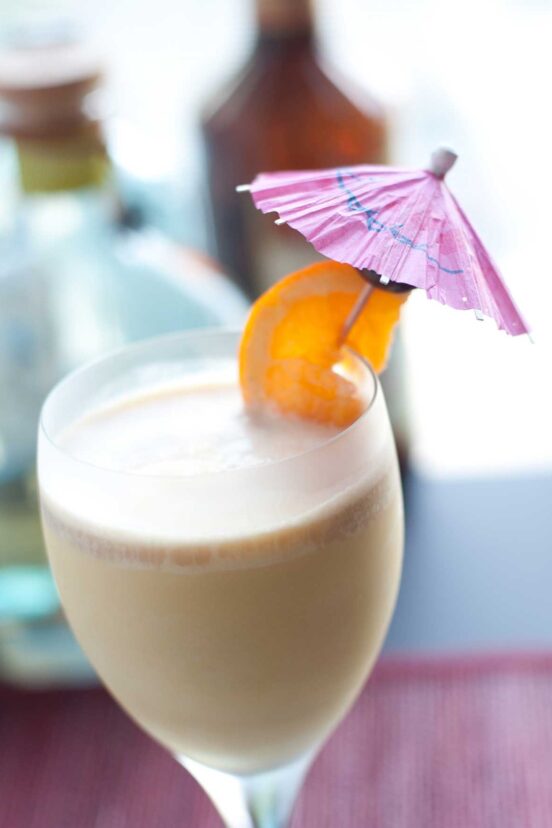 A wine glass filled with frozen Long Island iced tea, garnished with an orange slice on an umbrella.