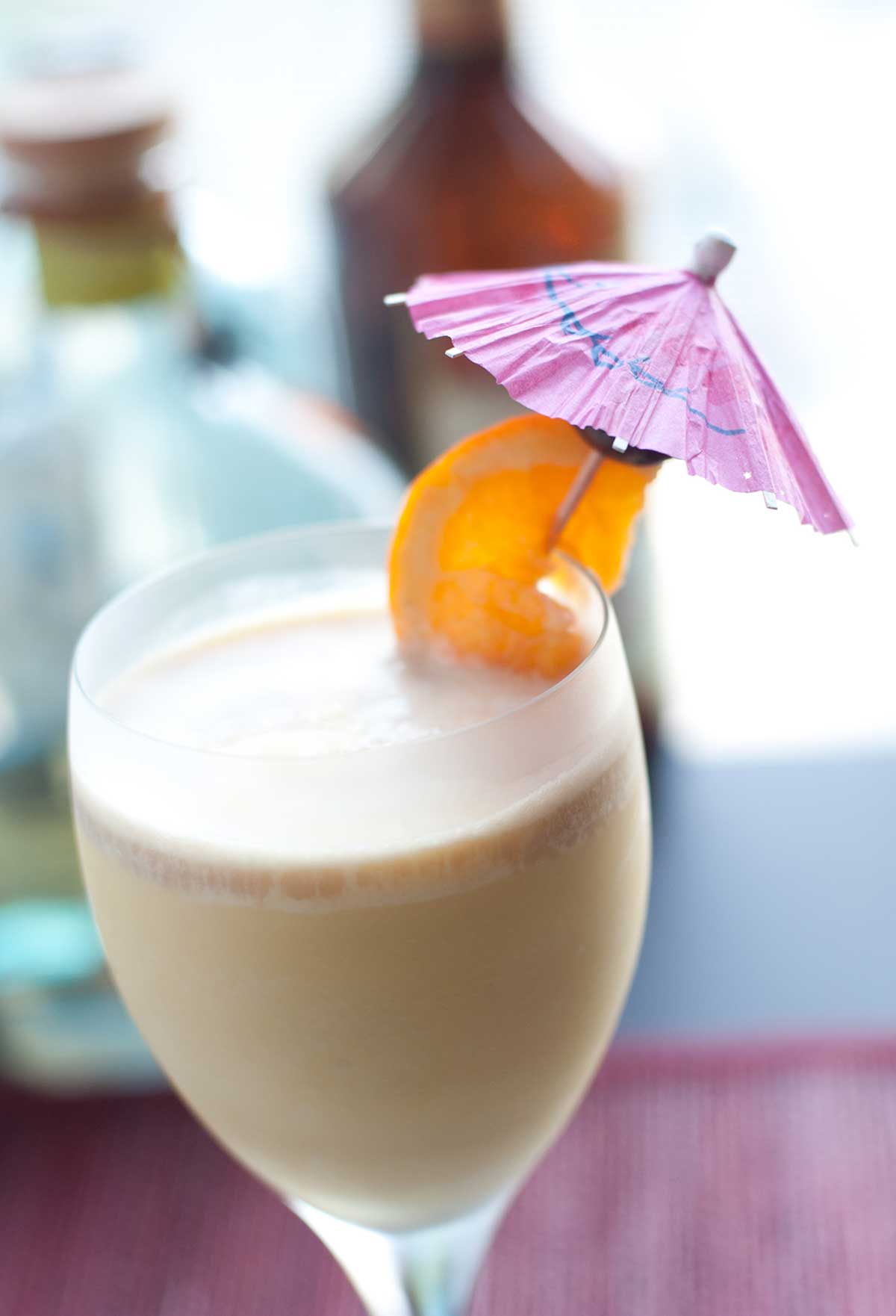 A wine glass filled with frozen Long Island iced tea, garnished with an orange slice on an umbrella.