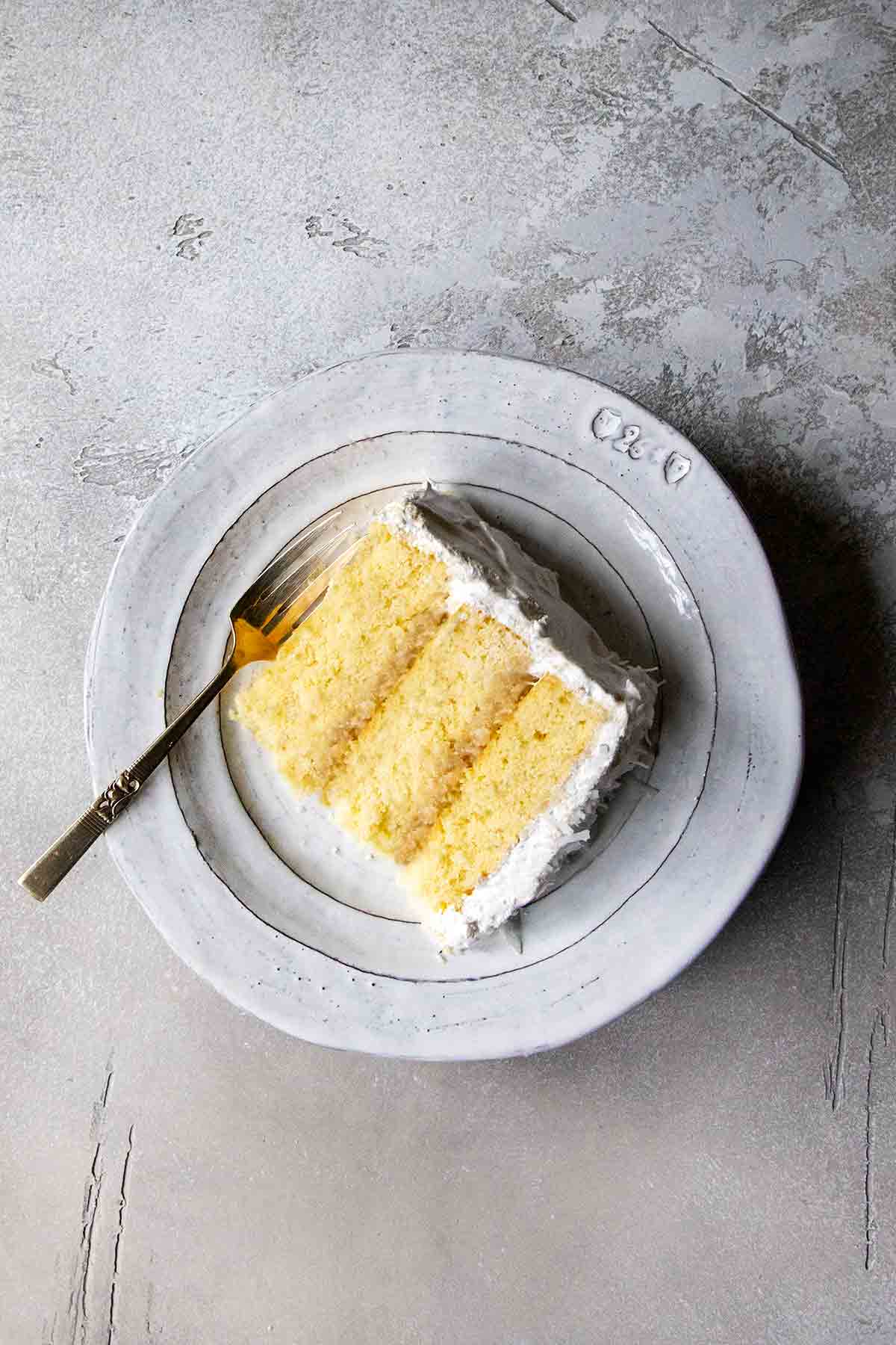 A slice of a three-layer coconut cake with white frosting on a gray plate.