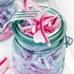 A canning jar overflowing with pickled red onions and a fork resting on the jar.