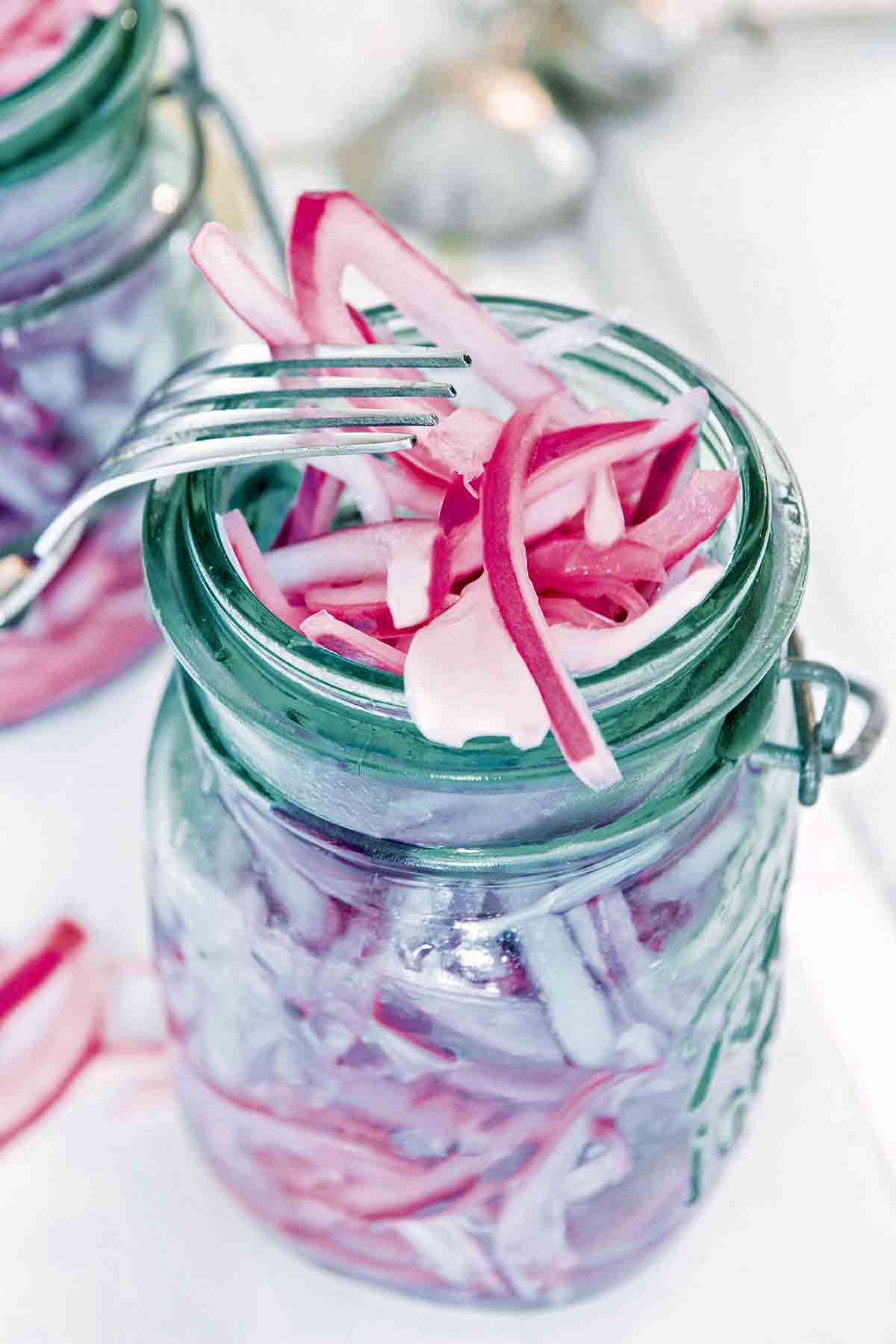 A canning jar overflowing with pickled red onions and a fork resting on the jar.