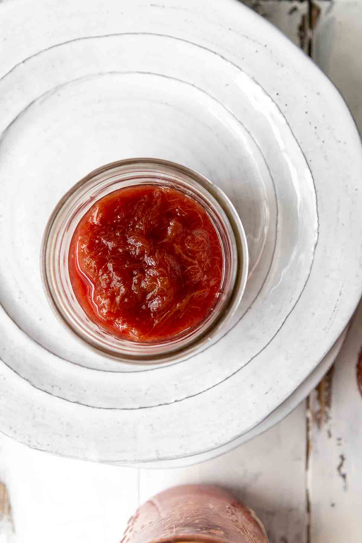 An overhead view of a jar of rhubarb jam on a white plate.