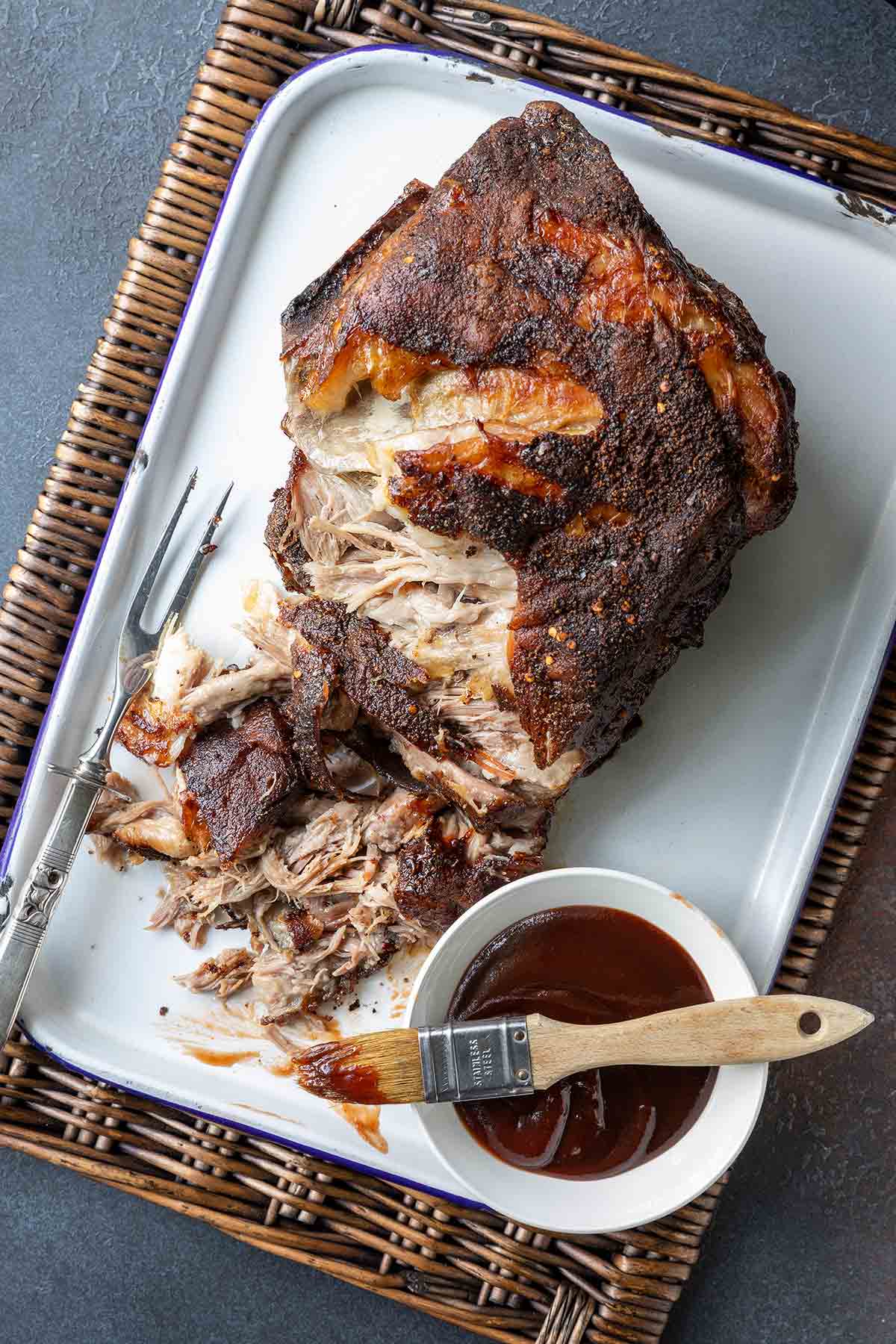 A partially shredded roast pork butt in a roasting pan with a fork nearby.