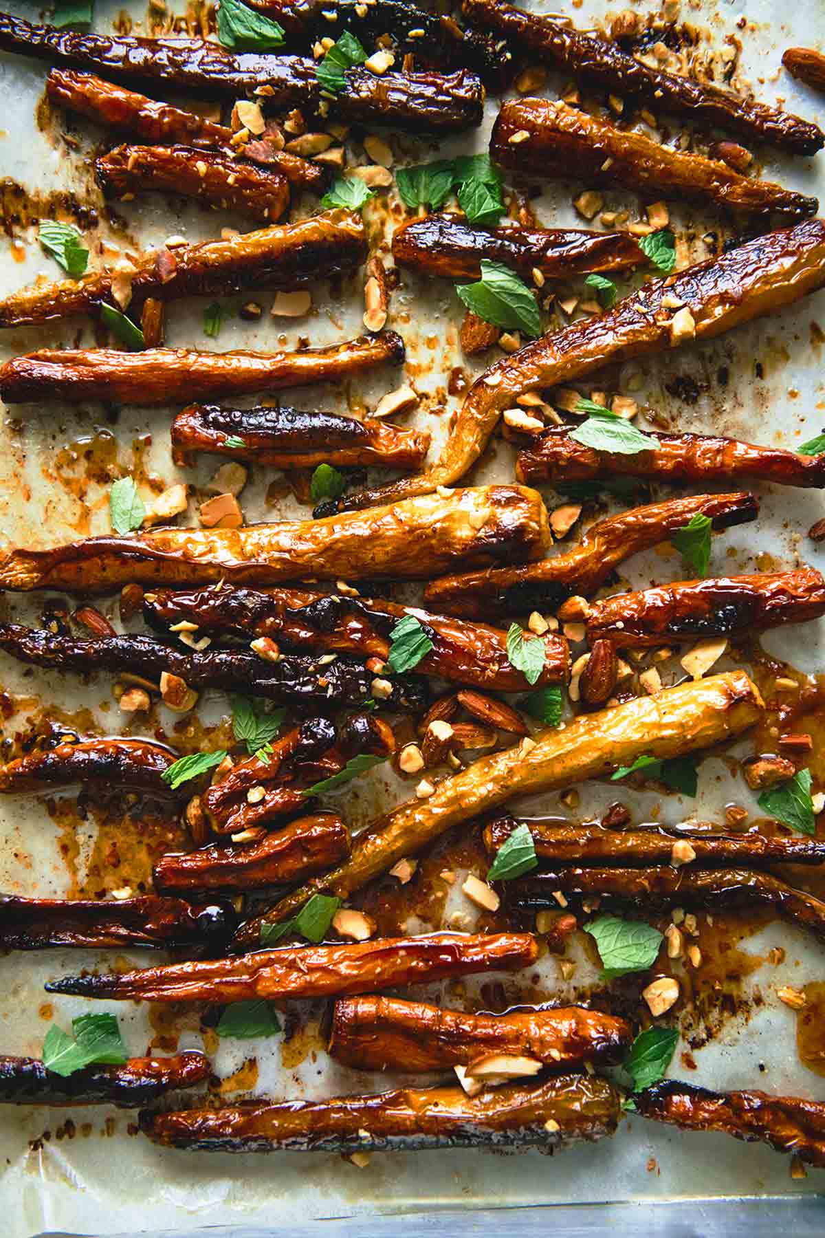 A rimmed baking sheet filled with roasted carrots with apricot glaze, chopped almonds, and torn mint.