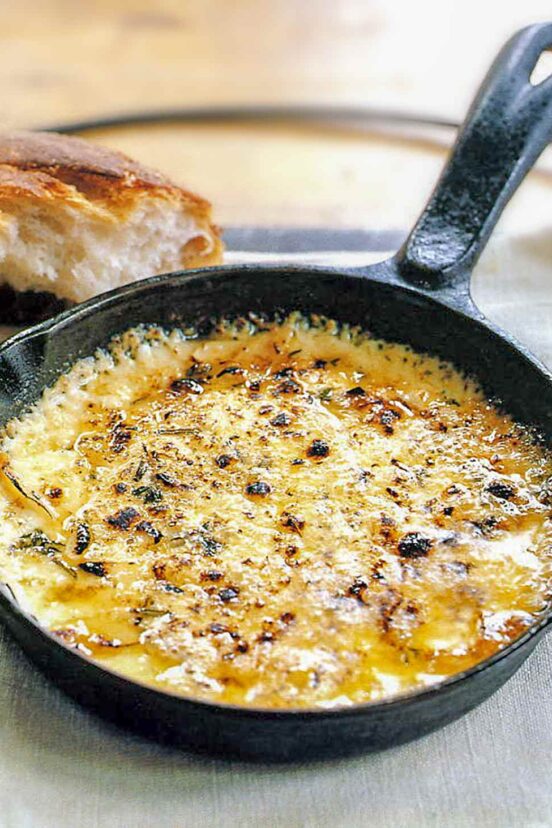 A small skillet filled with melted baked fontina with a chunk of bread next to it.