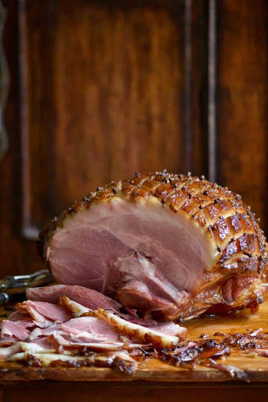 A partially carved mustard glazed ham on a wooden cutting board.
