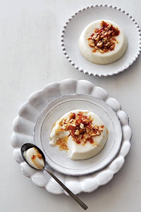 Two coconut panna cotta rounds on white dishes with a caramel nut topping.