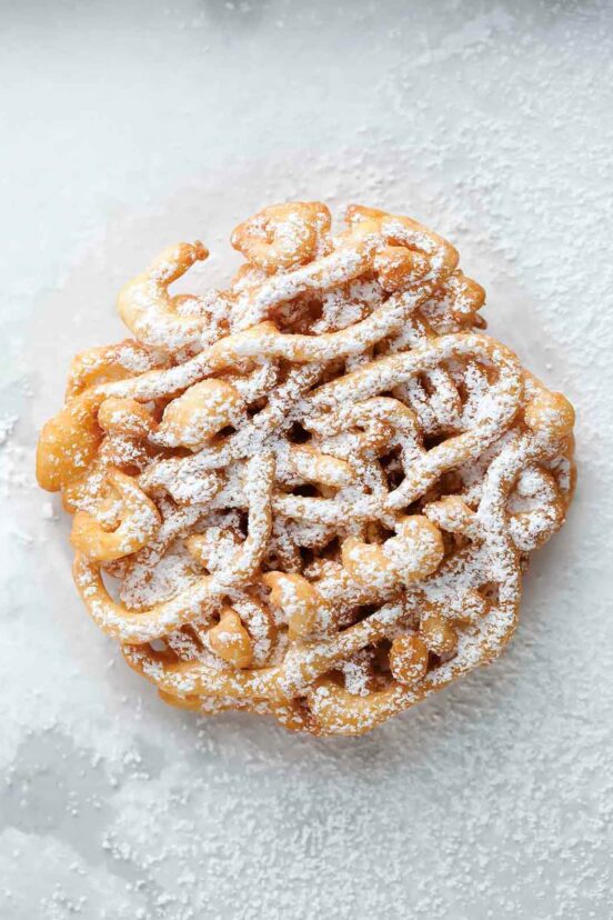 A fried mini funnel cake sprinkled with confectioners' sugar on a white background.