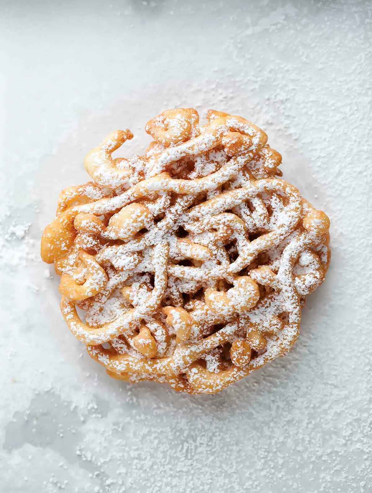 A fried mini funnel cake sprinkled with confectioners' sugar on a white background.