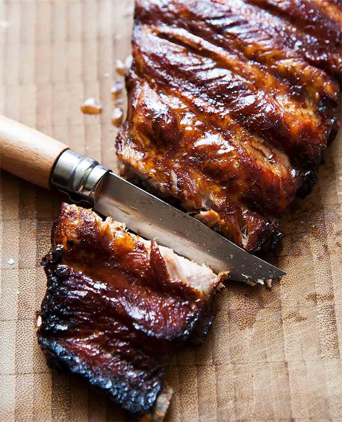 A knife cutting into a slab of pressure cooker ribs on a wooden board.