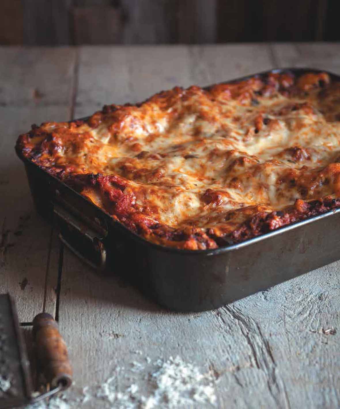 A rectangular baking dish filled with eggplant lasagna bolognese on a wooden table.