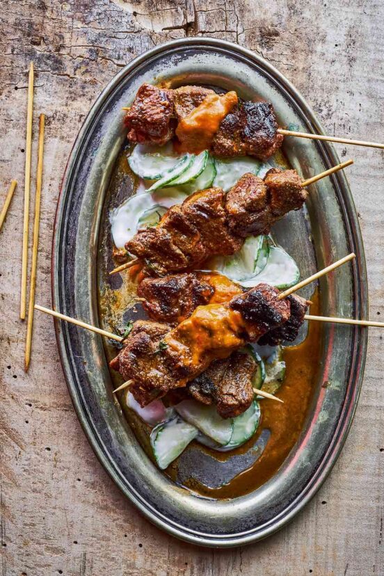 Five lamb skewers on top of creamy cucumber salad on an oval metal platter.