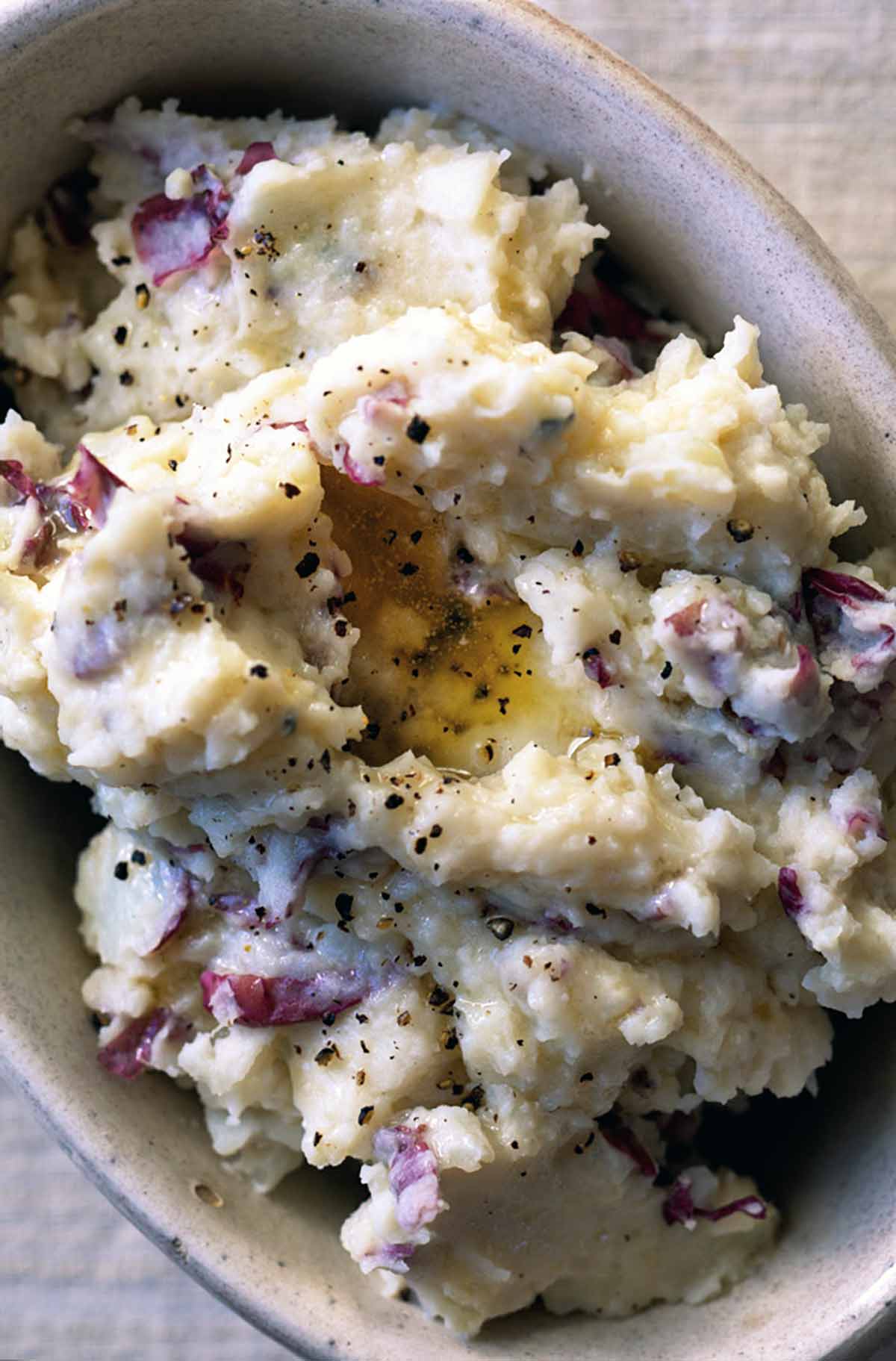 An oval dish filled with mashed red potatoes with cracked black pepper on top.