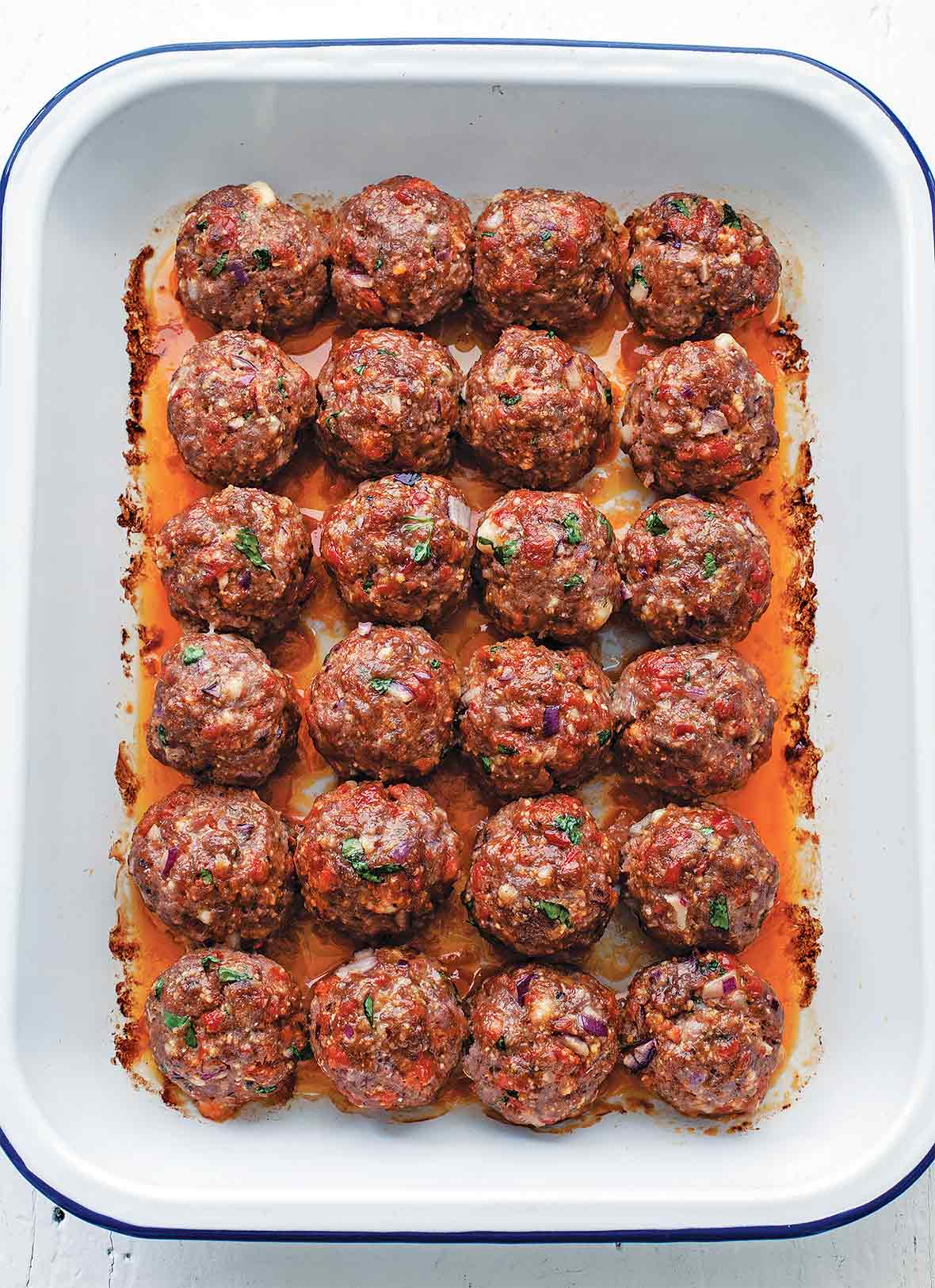 A white baking dish filled with 24 chorizo meatballs in even rows.