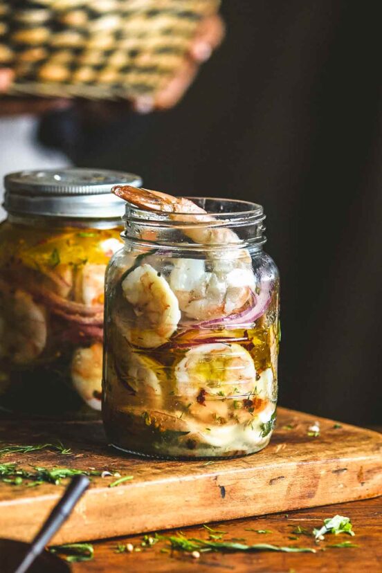 Two jars filled with pickled shrimp on a wooden cutting board.