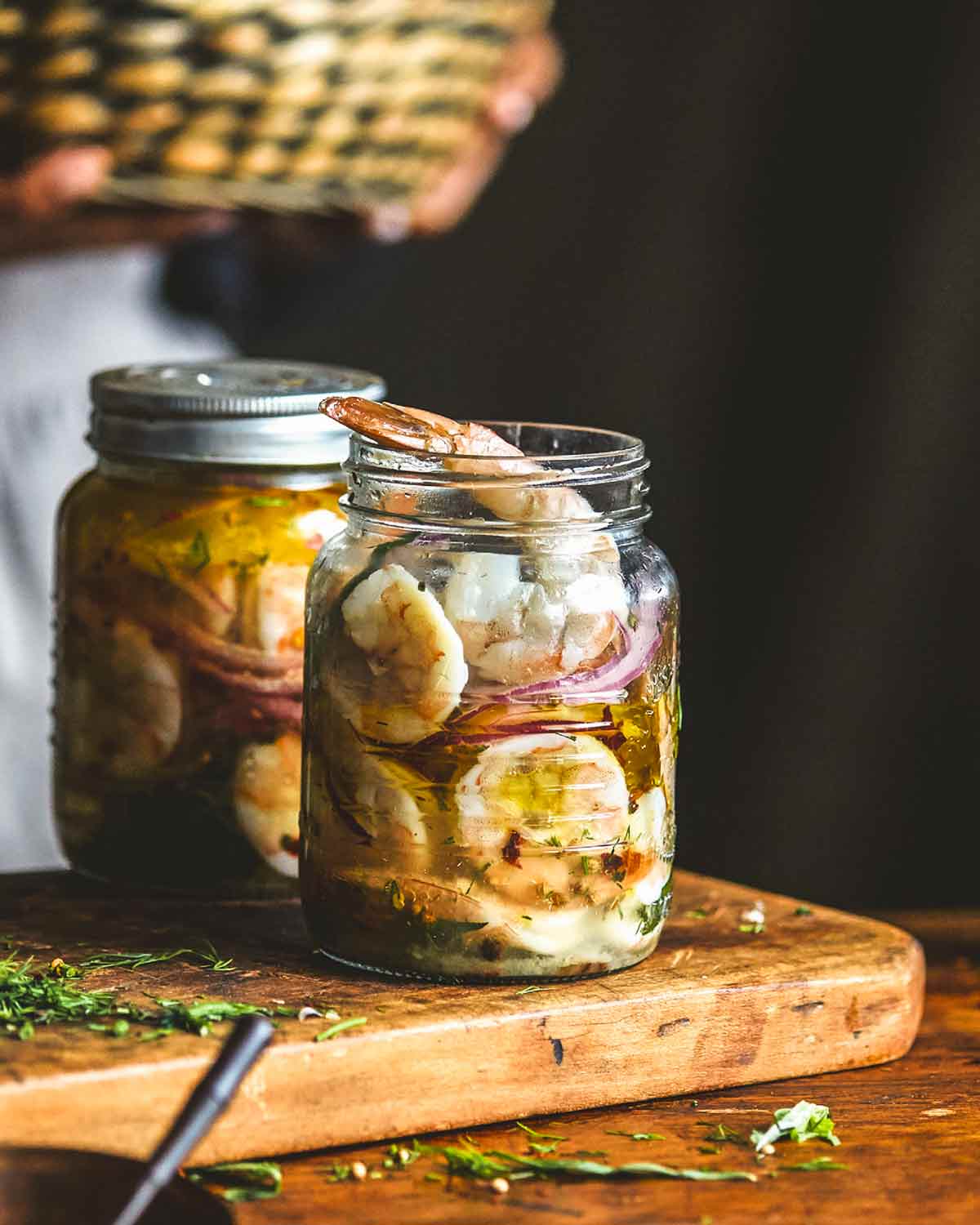Two jars filled with pickled shrimp on a wooden cutting board.