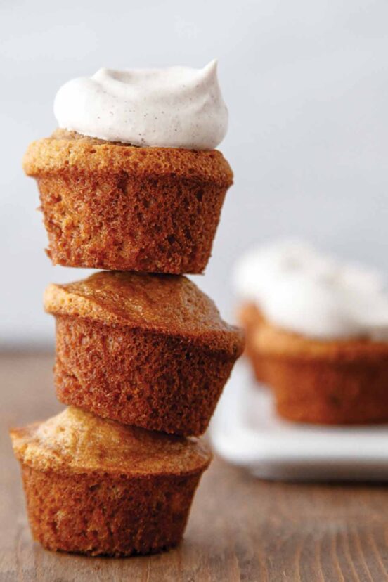 Three mini muffins stacked on top of each other with a dollop of spiced whipped cream on top.