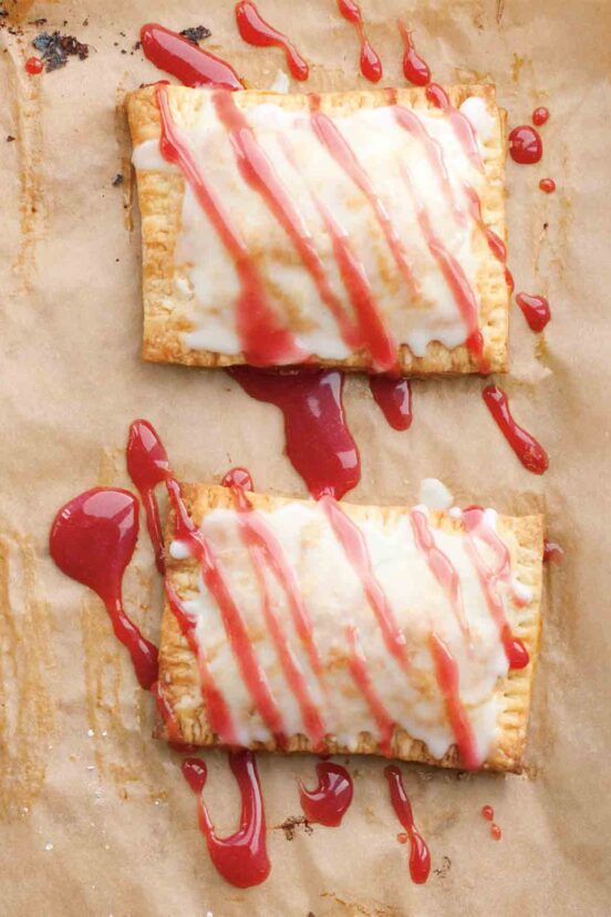 Two homemade pop tarts drizzles with a red syrup on a sheet of parchment.