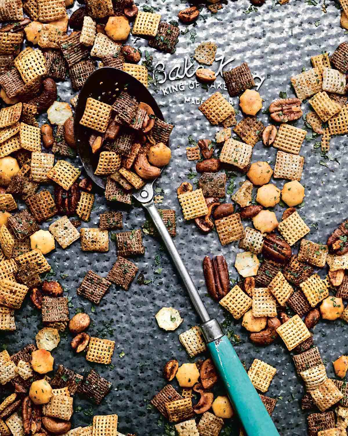 A tray of homemade Chex mix with a large spoon resting in the middle.