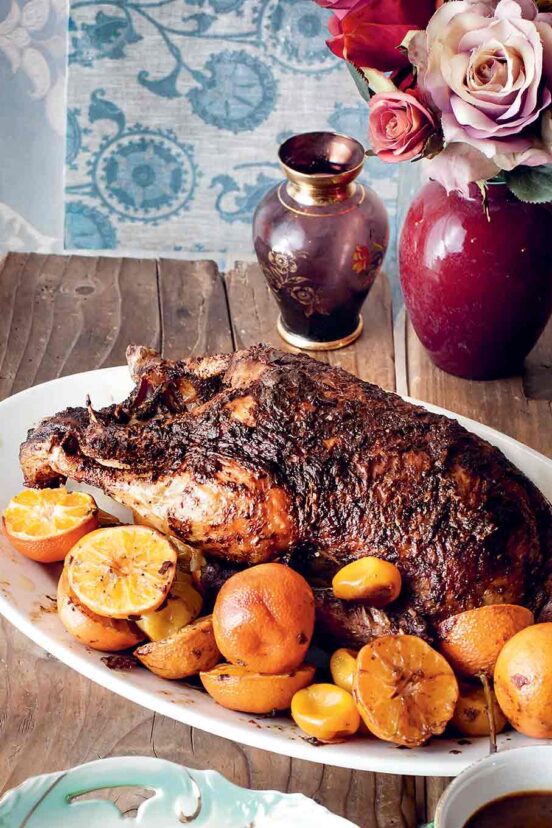 A whole roast duck on a platter, surrounded by halved clementines.