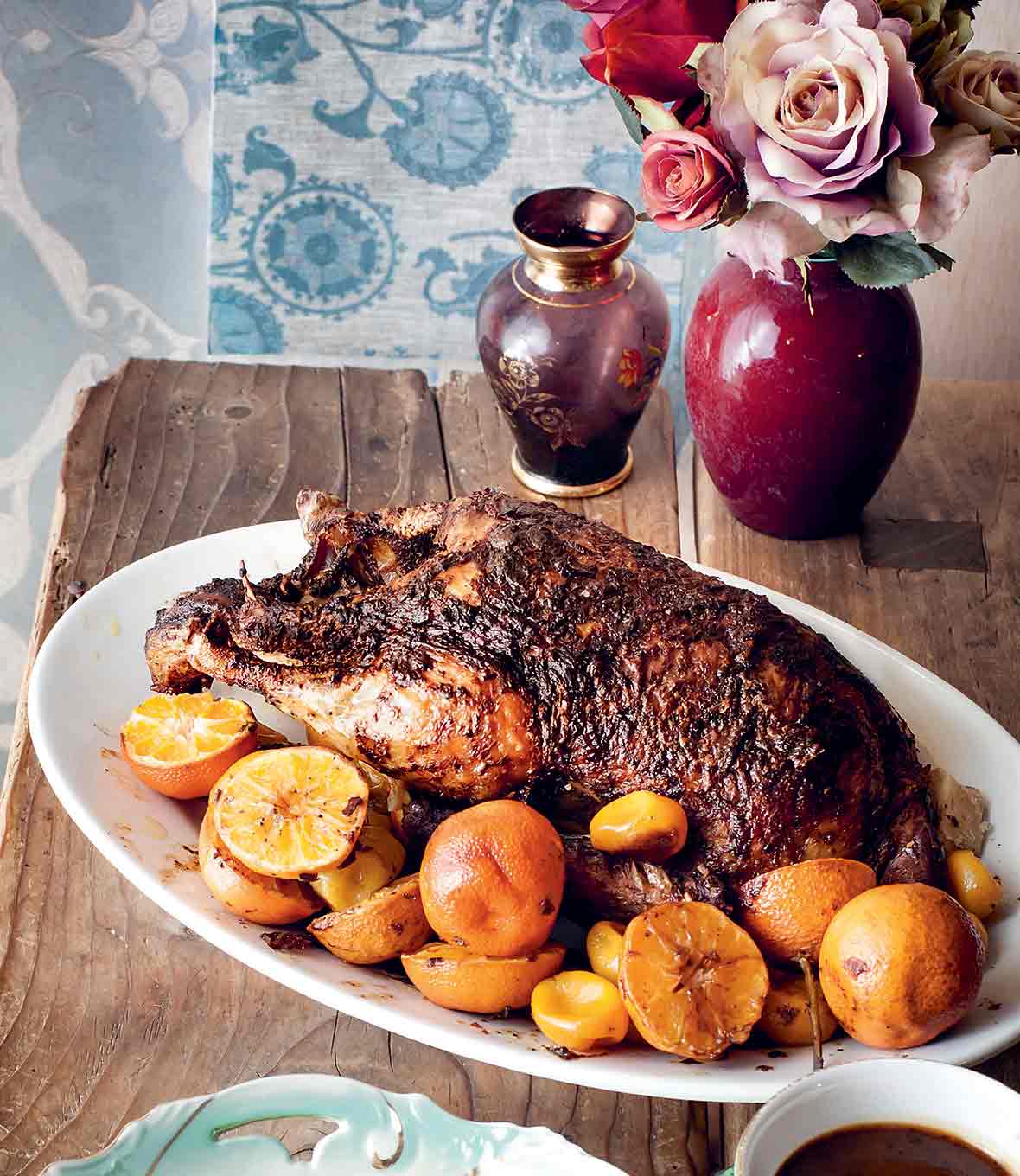 A whole roast duck on a platter, surrounded by halved clementines.