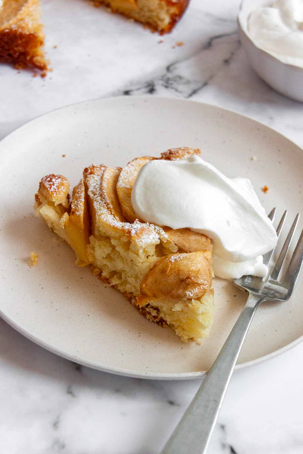 A slice of apple cake with a dollop of whipped cream on top.