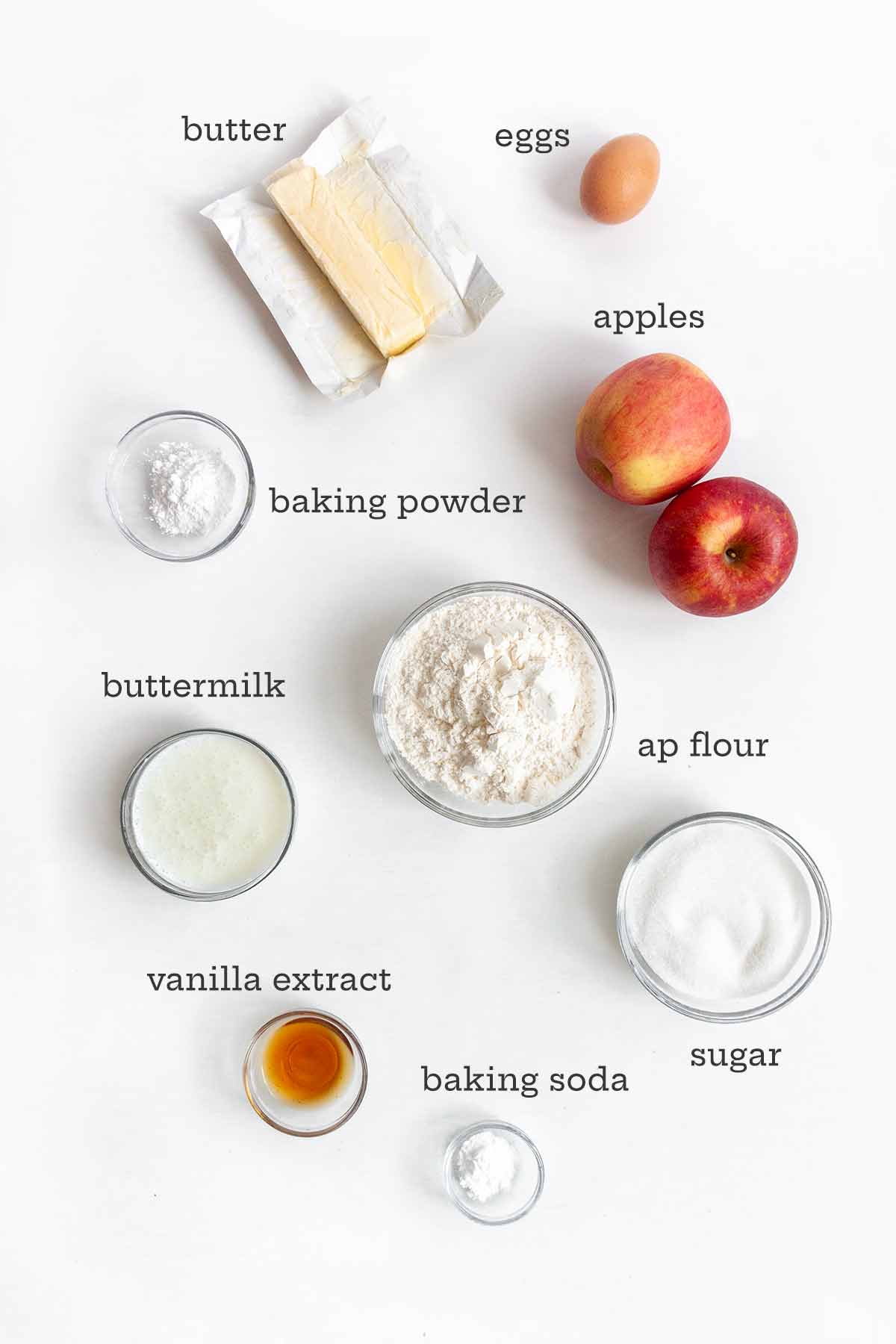 Ingredients for apple cake--butter, eggs, apples, baking powder, flour, buttermilk, sugar, vanilla, and baking soda.