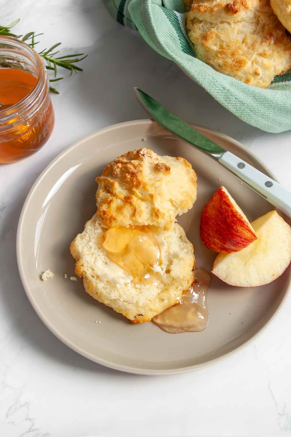 A plate with a cut apple and a biscuit split in half and topped with apple jelly.