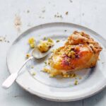 Plate with an slice of apricot tart filled with frangipane and topped with chopped pistachios.