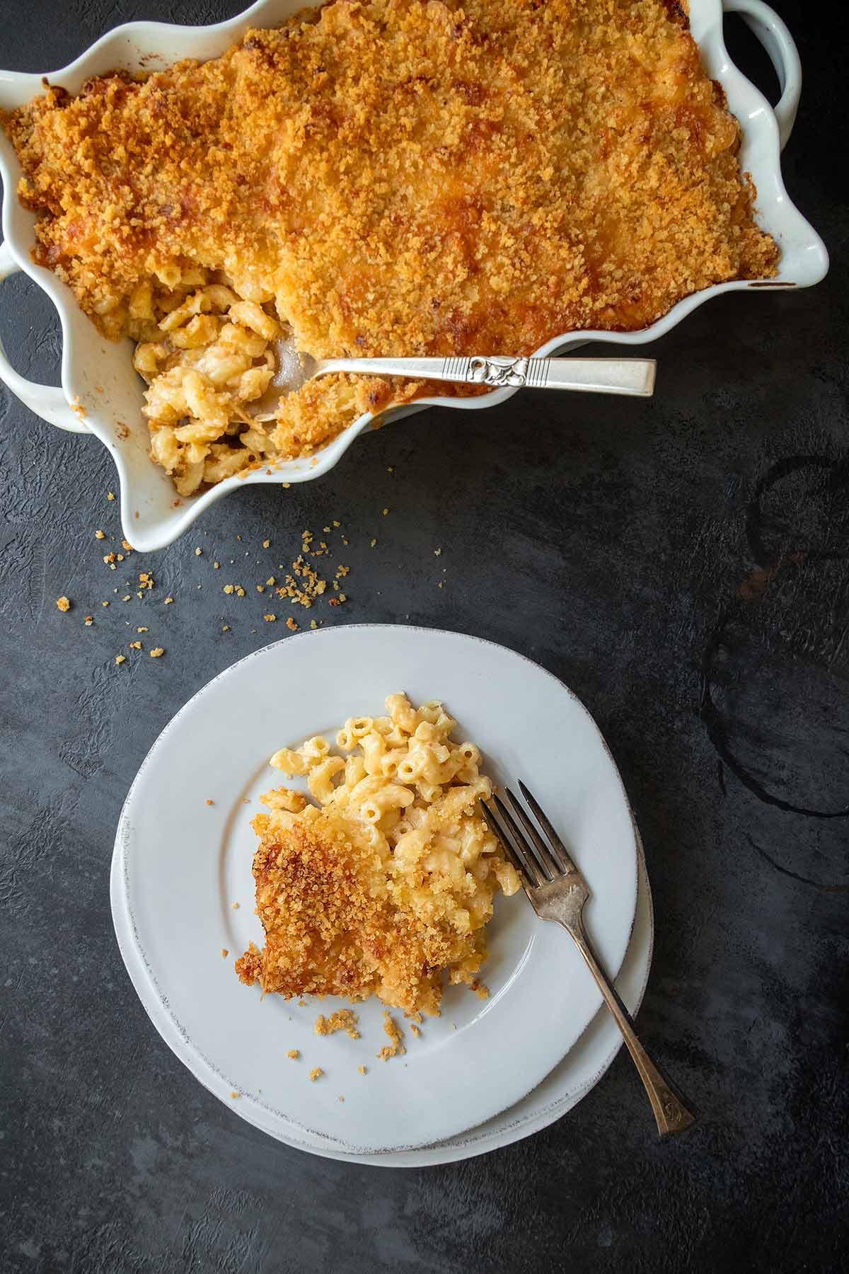 A casserole dish of mac and cheese with a plate with a portion of the pasta.