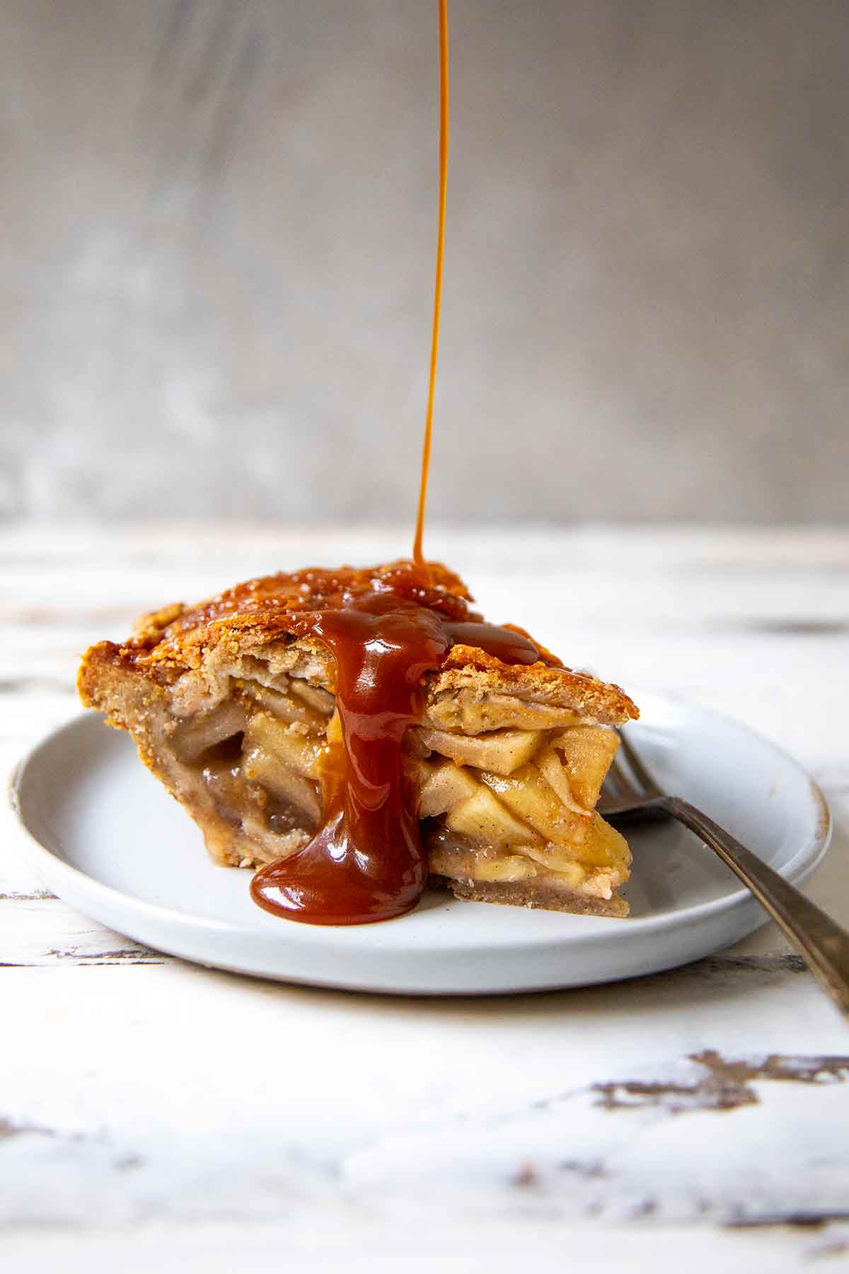 Caramel sauce drizzled over a slice of apple pie on a white plate.