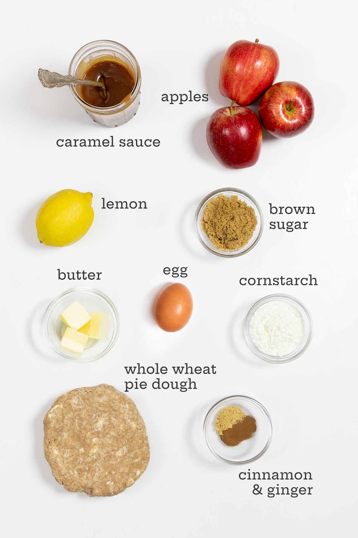 Ingredients for caramel apple pie--caramel sauce, apples, lemon, brown sugar, butter, cornstarch, egg, pie dough, and cinnamon and ginger.