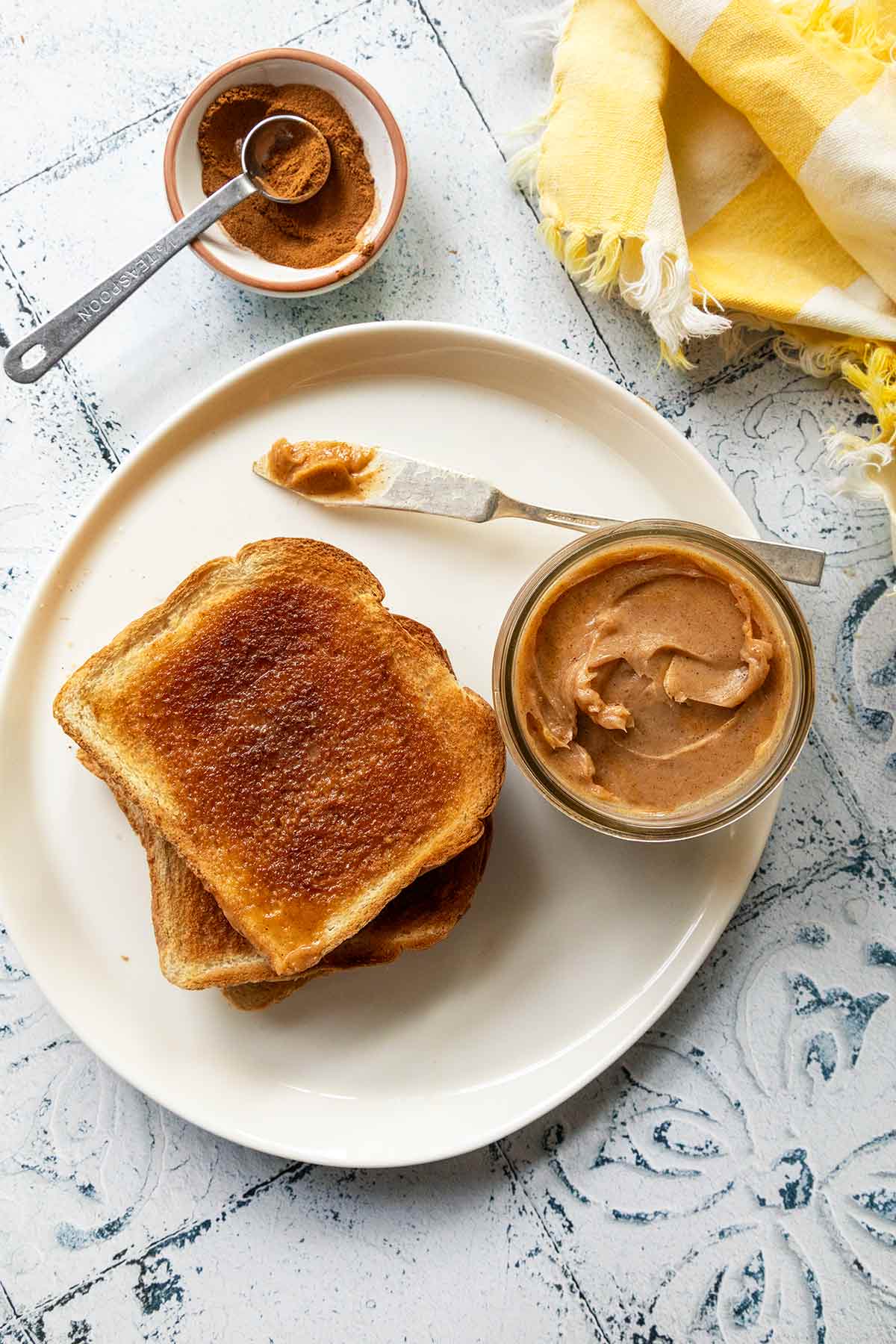 A bowl of cinnamon butter on a white plate with two slices of toast and a knife beside it.