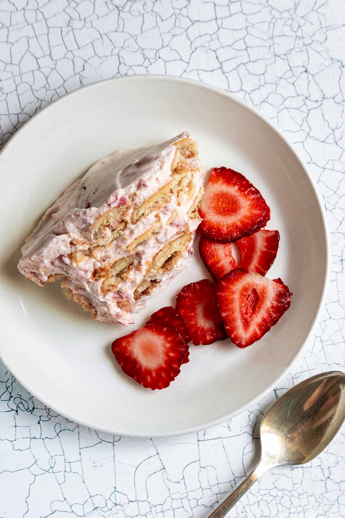 A serving of strawberry icebox cake on a plate with sliced strawberries and a spoon on the side.