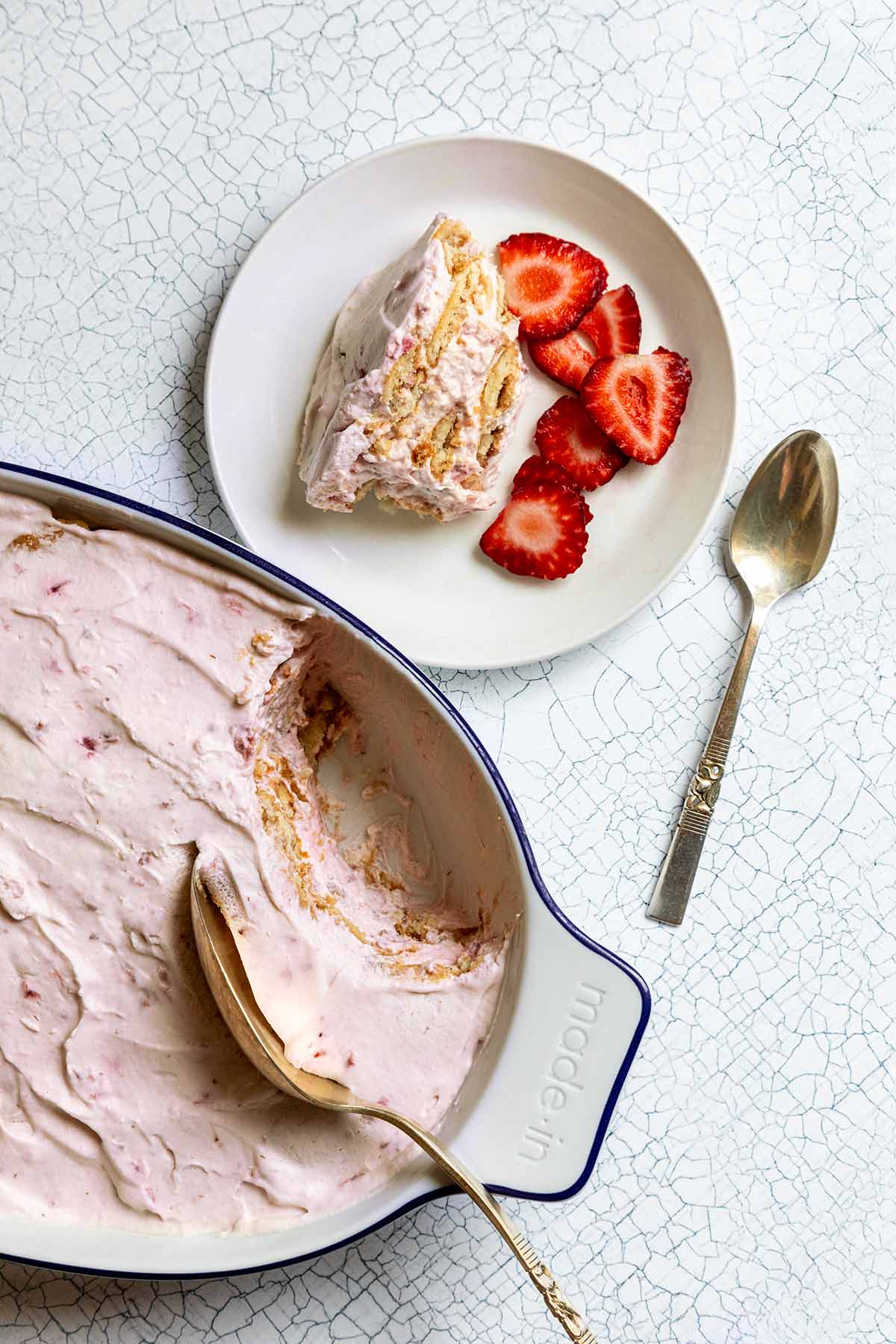 A serving of strawberry icebox cake next to an oval baking dish filled with the remaining dessert.