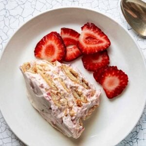 A serving of strawberry icebox cake next to an oval baking dish filled with the remaining dessert.