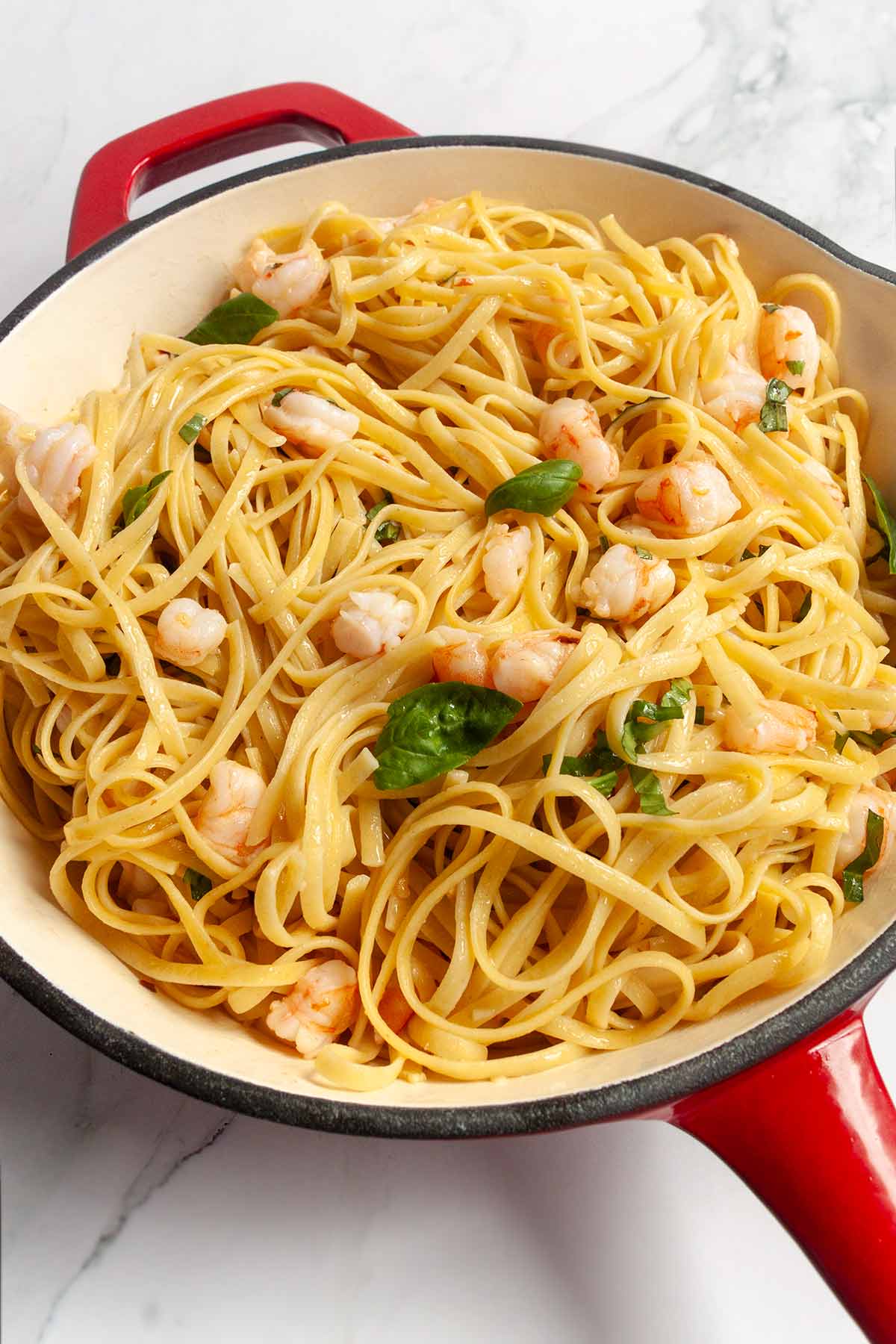 A tangle of pasta and shrimp topped with fresh basil in a red skillet.