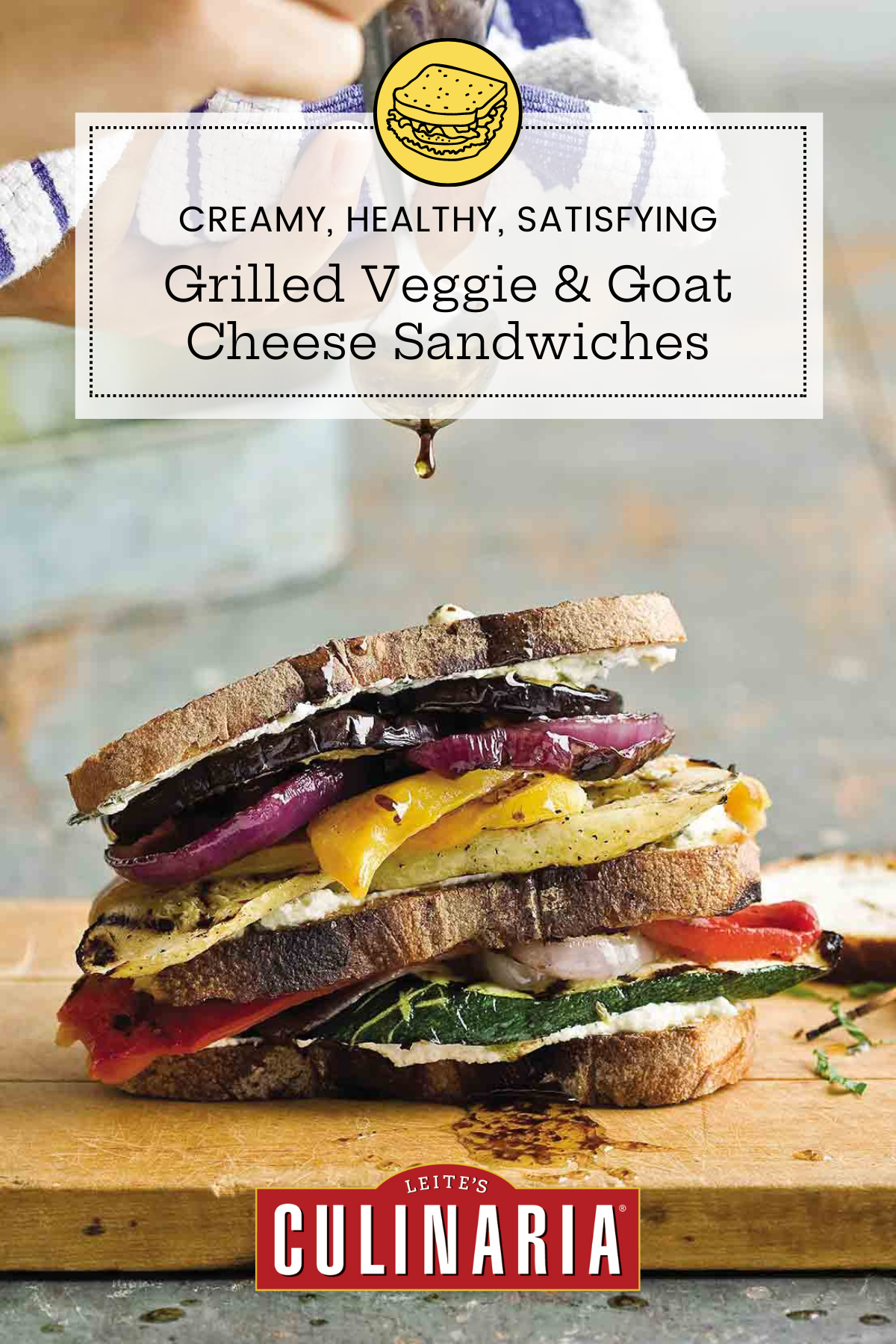 A grilled vegetable and goat cheese sandwich, made with grilled onion, eggplant, and squash on a cutting board being drizzled with balsamic vinaigrette.