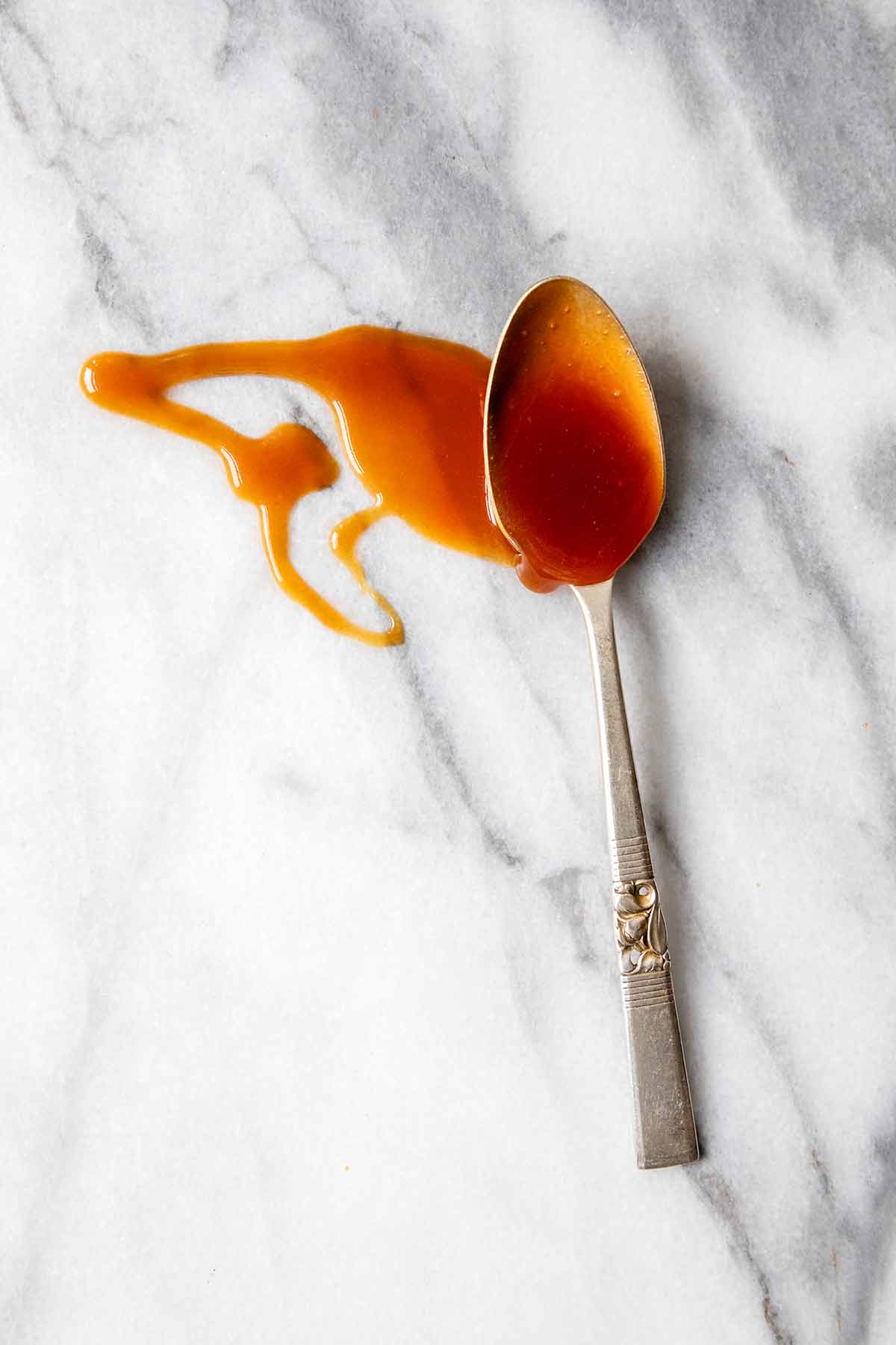 A spoonful of caramel sauce dripped onto a marble surface.