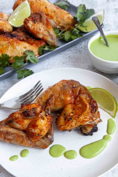 Two pieces of Peruvian chicken on a white plate with green sauce and a lime wedge.