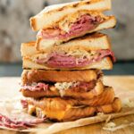 A stack of halved reuben sandwiches on a wooden cutting board.